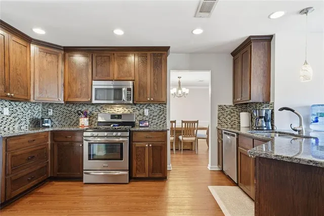 a kitchen with stainless steel appliances granite countertop wooden cabinets a sink dishwasher a stove and a refrigerator with wooden floor