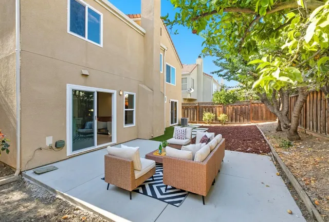 a view of a patio with couches and a table and chairs with wooden fence and large trees