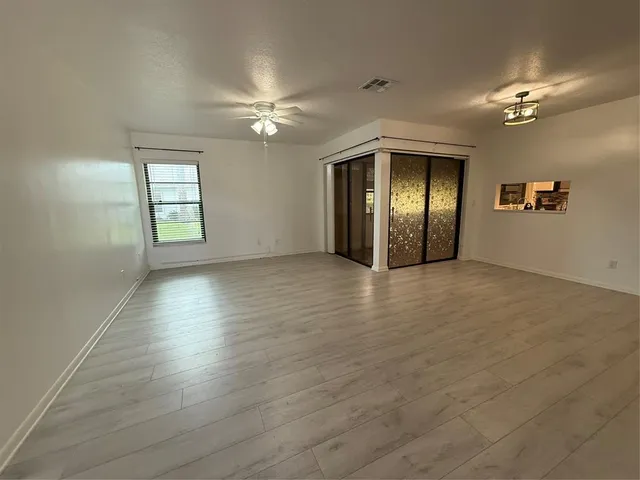 an empty room with wooden floor chandelier and windows