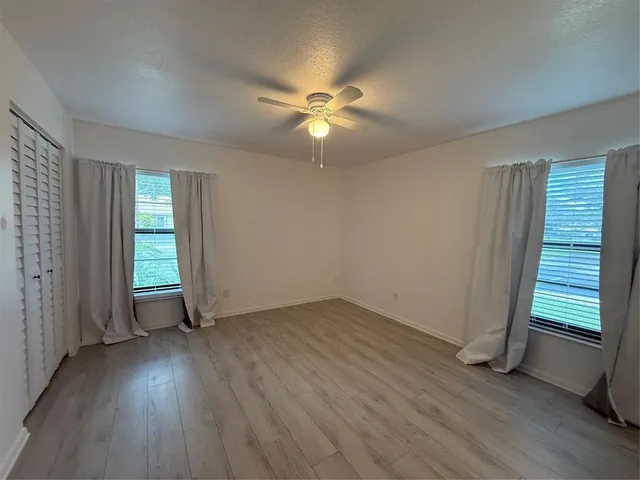 an empty room with wooden floor closet fan and windows