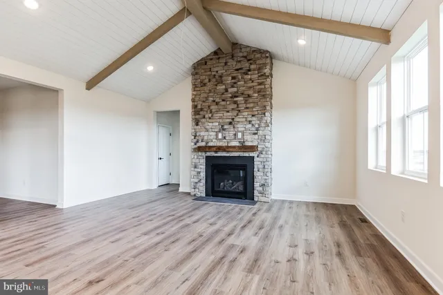 an empty room with wooden floor fireplace and windows