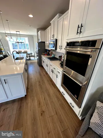 a kitchen with stainless steel appliances a stove a sink a microwave a refrigerator a stove and white cabinets with wooden floor