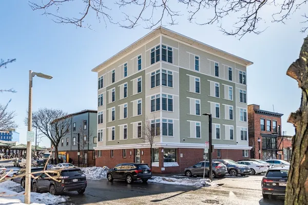 a front view of a building with lot of cars and trees