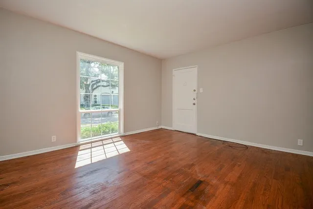 a view of an empty room with wooden floor and a window