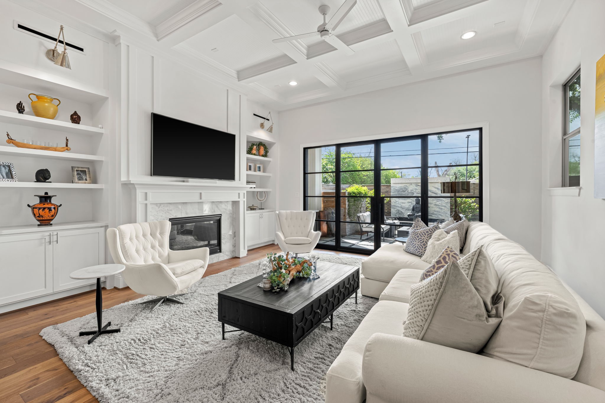 110 East 26th Street, Unit B Houston, TX 77008 - Photo 12 of 43 This gorgeous living room is centered around a fireplace with a marble surround and custom mantel, flanked by elegant built-ins. The upgraded tray ceiling adds a refined layer to the space, while the layout offers a direct view of the impactful steel-and-glass doors and the backyard oasis beyond. It is a perfectly composed room that balances high-end custom details with a relaxing, outdoor-connected energy.