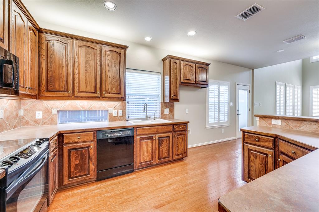 3912 Sovereign Drive Bedford, TX 76021 - Photo 11 of 34 Kitchen with tasteful backsplash, black appliances, solid wood flooring, brown cabinets, and recessed lighting