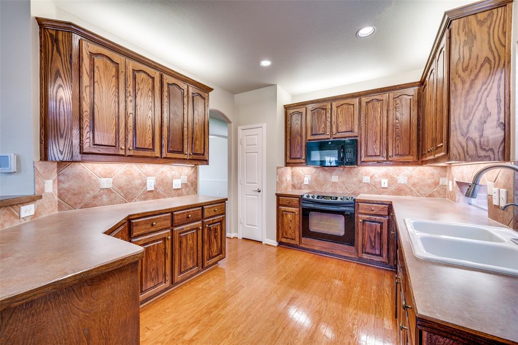 3912 Sovereign Drive Bedford, TX 76021 - Photo 10 of 34 Kitchen with tasteful backsplash, black appliances, solid wood flooring, brown cabinets, and recessed lighting