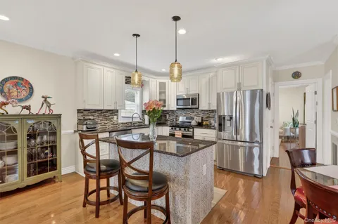 a kitchen with stainless steel appliances granite countertop a refrigerator a stove a sink dishwasher and a dining table with wooden floor