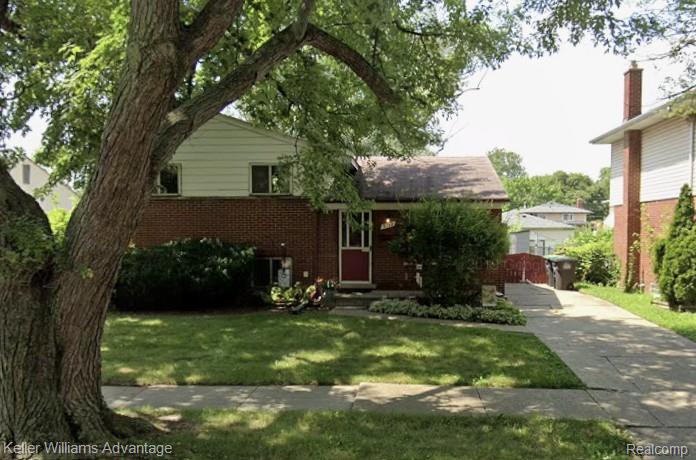 9782 William Street Taylor, MI 48180 - Photo 1 of 1 Brick and siding exterior featuring a red entry door, a paved driveway, and a front lawn with mature trees and shrubbery
