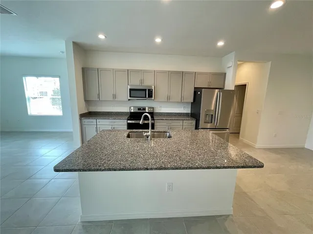 a kitchen with kitchen island granite countertop a stove a sink a refrigerator a counter top space and cabinets