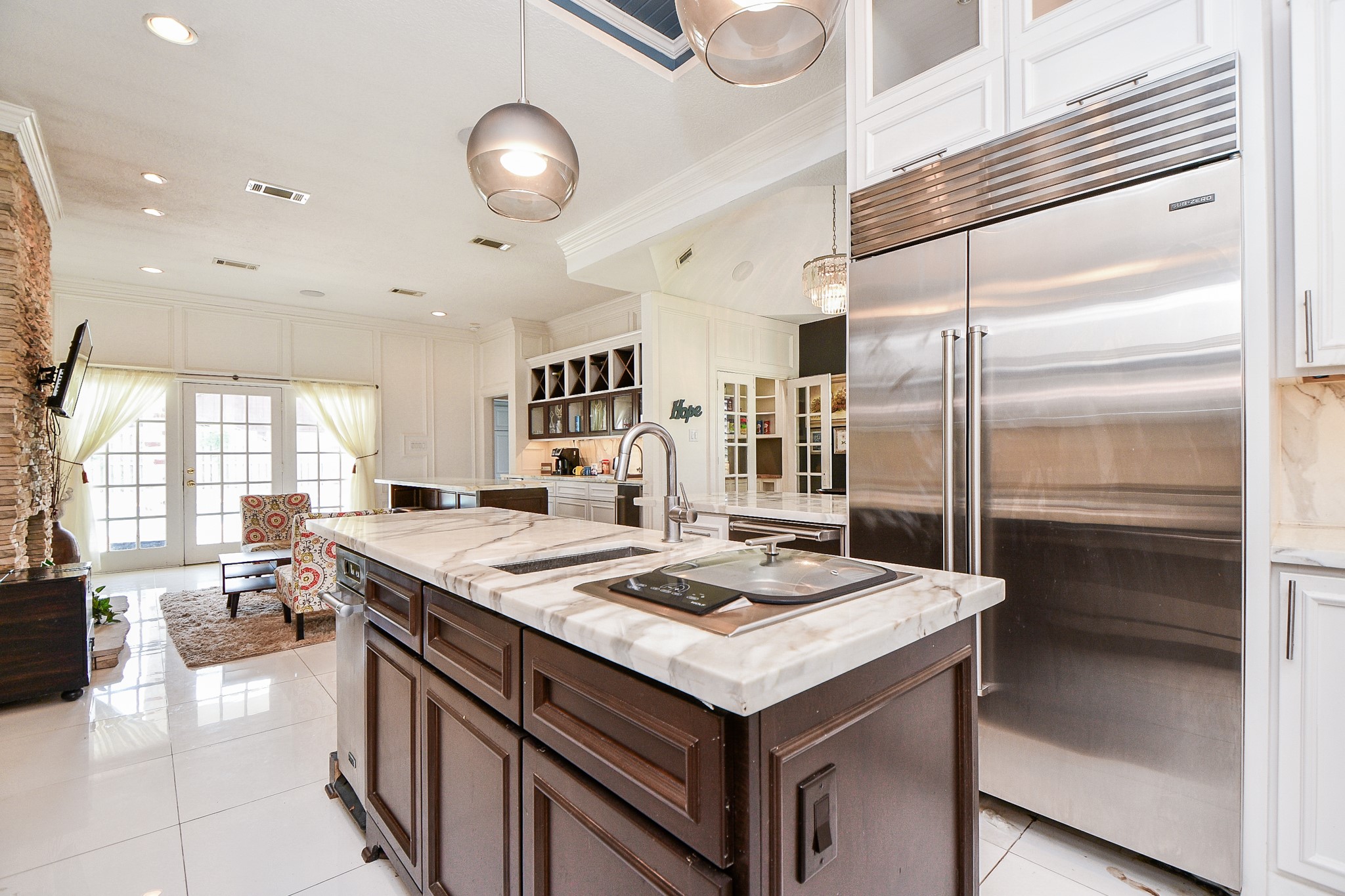 263 Wood Loop Street Houston, TX 77015 - Photo 16 of 45 This photo showcases a spacious, modern kitchen with a large island featuring marble countertops, stainless steel appliances, and ample cabinet space. The open layout flows into a cozy living area with natural light streaming through glass doors, creating a welcoming atmosphere.