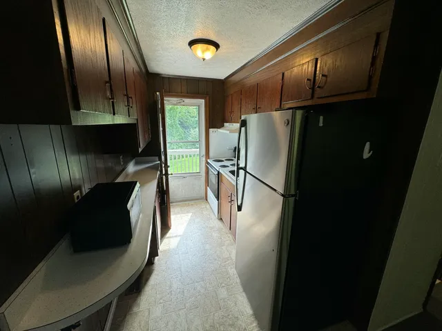 a view of a refrigerator in kitchen and an empty room with wooden floor