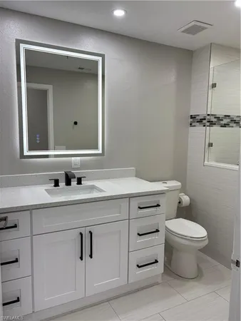 a bathroom with a granite countertop toilet sink vanity and mirror