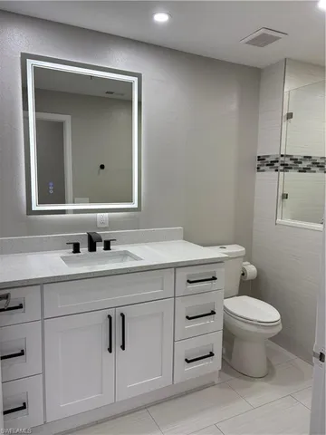 a bathroom with a granite countertop toilet sink vanity and mirror