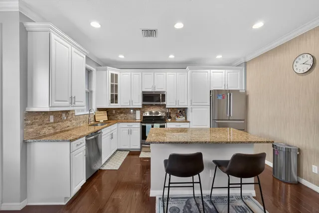 a kitchen with stainless steel appliances granite countertop a stove top oven a sink a refrigerator and white cabinets with wooden floor