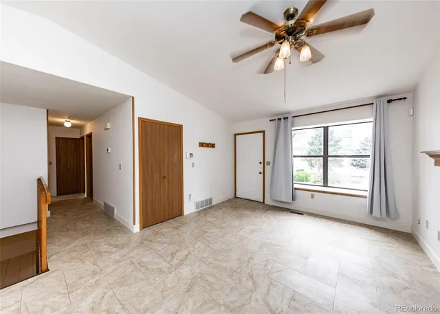an empty room with chandelier fan and windows