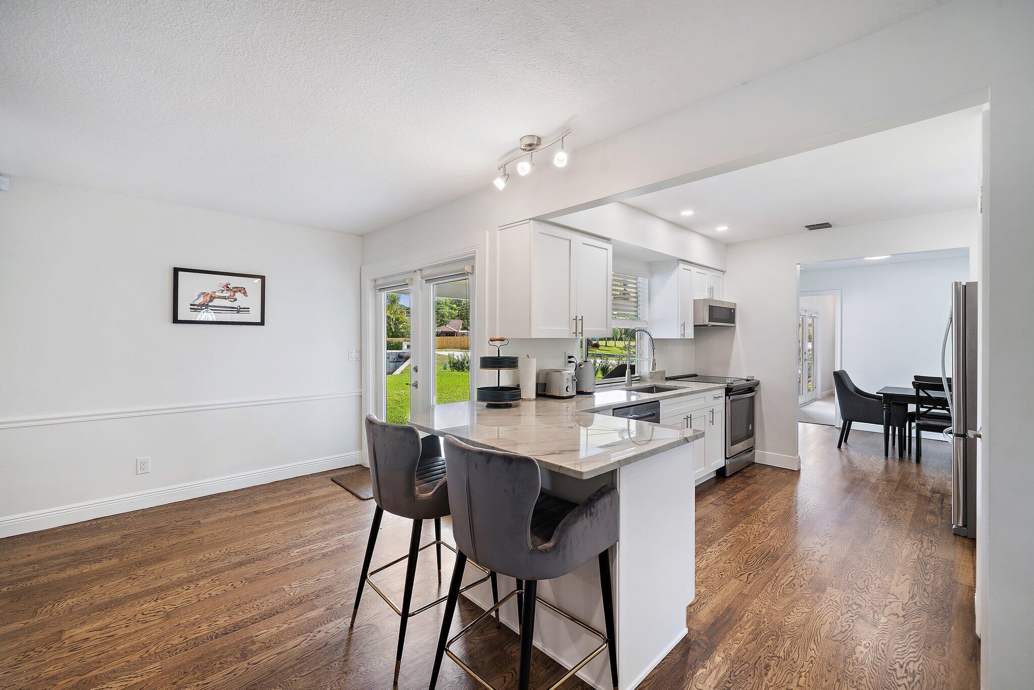 1342 Essex Drive Wellington, FL 33414 - Photo 28 of 58 a kitchen with a dining table chairs wooden floor and appliances