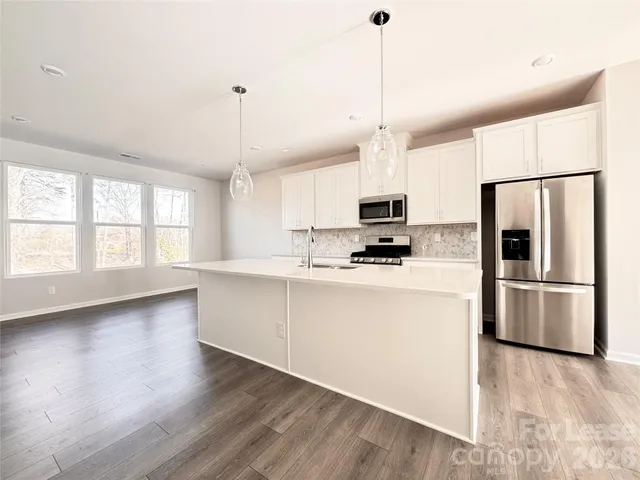 a kitchen with stainless steel appliances granite countertop a refrigerator a oven a white counter space and wooden floor