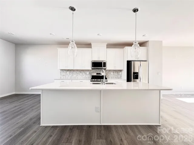 a kitchen with stainless steel appliances granite countertop a sink a microwave a refrigerator and white cabinets