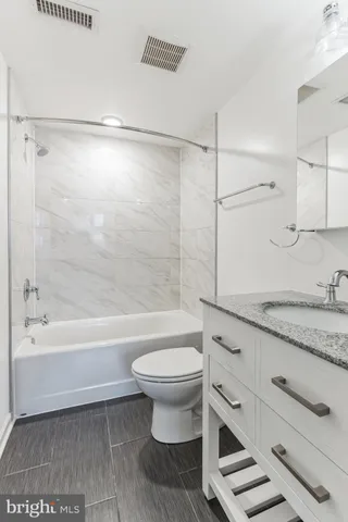 a bathroom with a granite countertop sink toilet a mirror and a bathtub