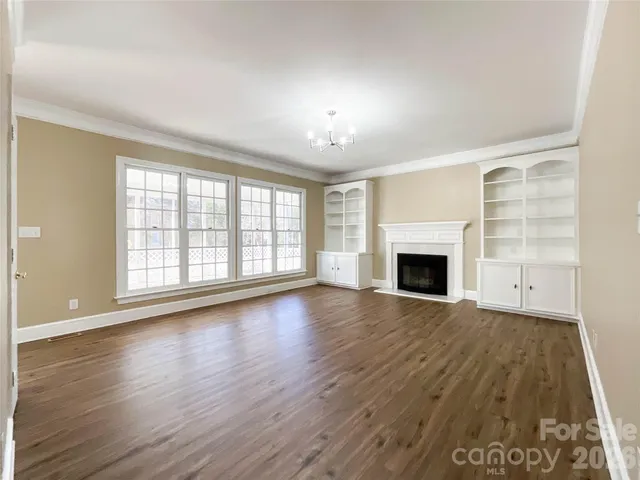 an empty room with wooden floor fireplace and windows