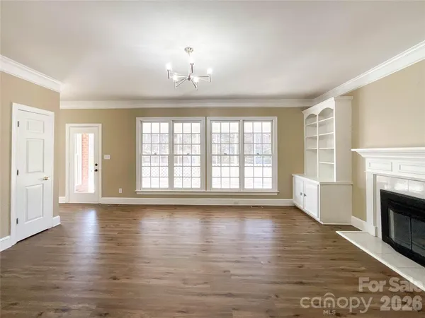 an empty room with wooden floor fireplace and windows