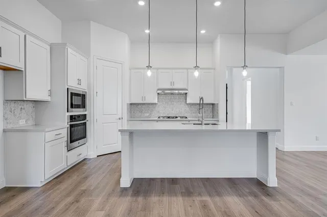 a kitchen with stainless steel appliances granite countertop a sink a stove a refrigerator and white cabinets with wooden floor