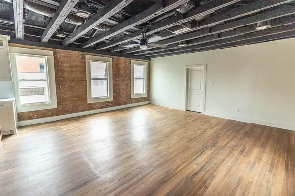 a view of an empty room with wooden floor and windows
