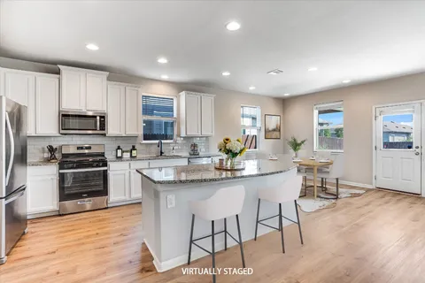 a kitchen with stainless steel appliances granite countertop a stove top oven a sink dishwasher a dining table and chairs with wooden floor