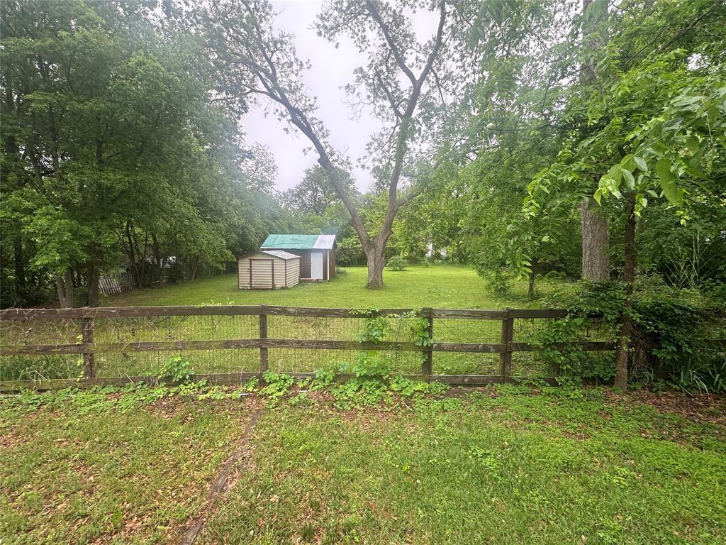 504 1st Street Terrell, TX 75160 - Photo 25 of 27 Expansive green space featuring two storage sheds, a mature tree, and a wooden fence