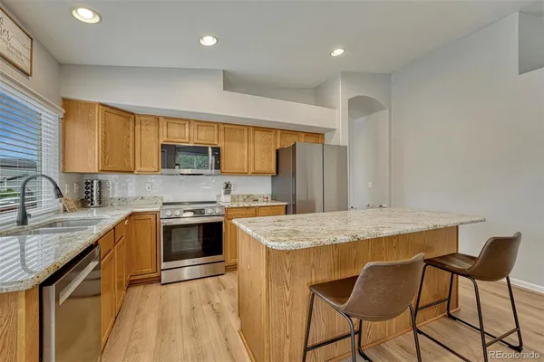 a kitchen with stainless steel appliances granite countertop a sink a stove a refrigerator cabinets a dining table and chairs