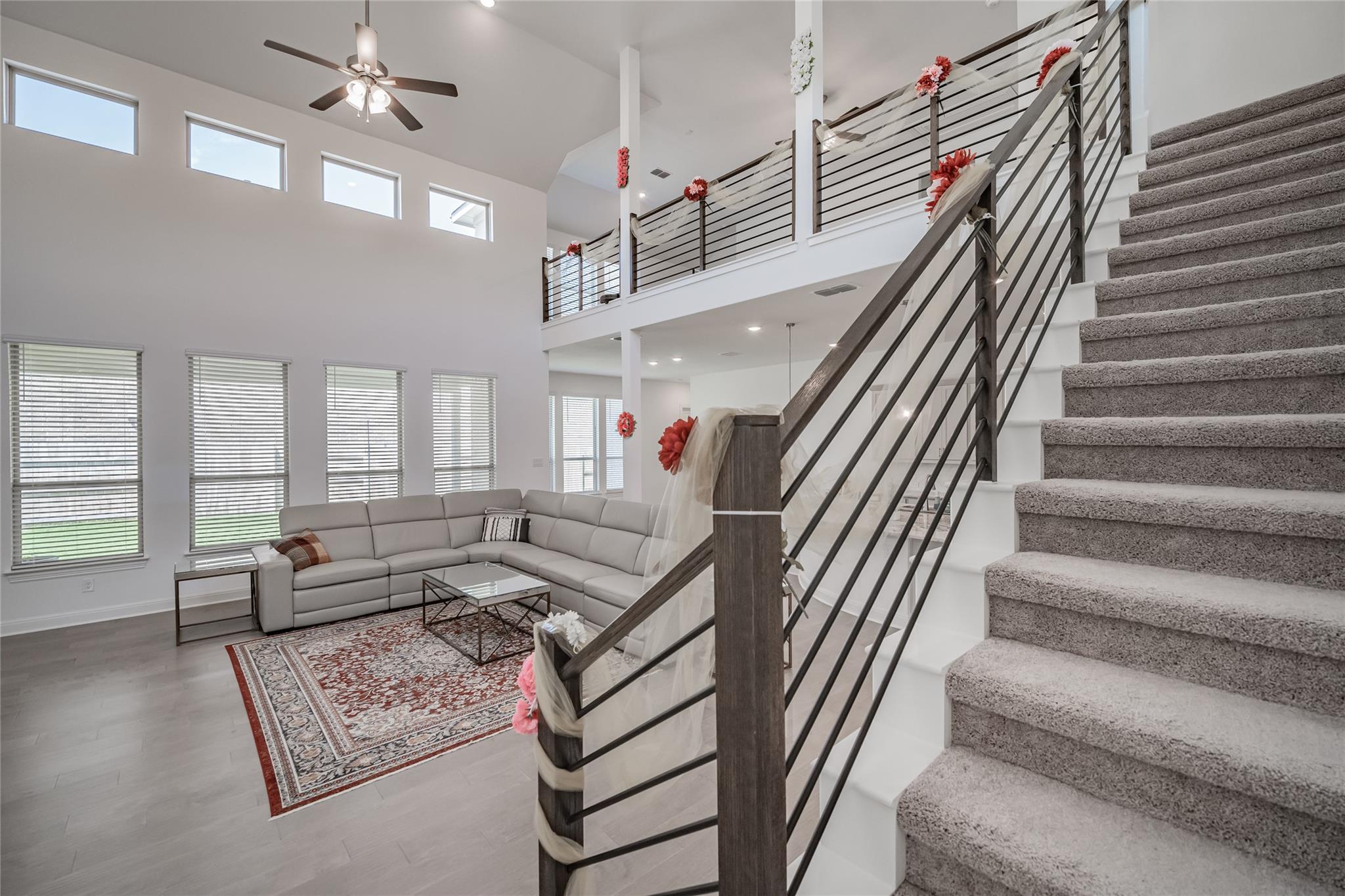 3049 Sage Ranch Drive Leander, TX 78641 - Photo 7 of 23 A grand staircase with modern railings ascends to a loft overlooking the living area with high ceilings and abundant windows.
