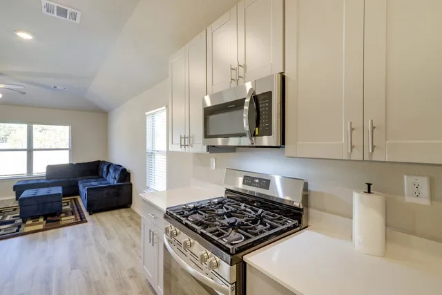 a kitchen with stainless steel appliances granite countertop a stove and a view of living room