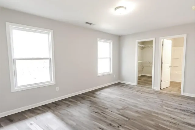 an empty room with wooden floor closet and windows