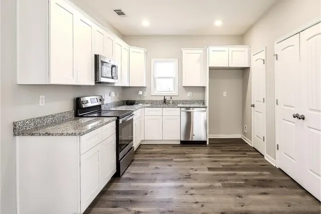 a kitchen with stainless steel appliances granite countertop a stove top oven a refrigerator a sink and white cabinets