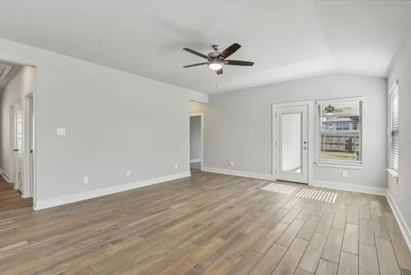 an empty room with wooden floor a ceiling fan and windows