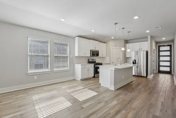 a large kitchen with stainless steel appliances granite countertop a stove a sink a refrigerator white cabinets and wooden floor next to a window