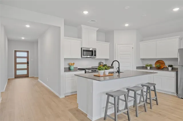 a kitchen with stainless steel appliances granite countertop a stove top oven a sink a dining table and chairs with wooden floor