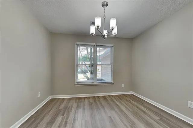 an empty room with wooden floor chandelier and windows