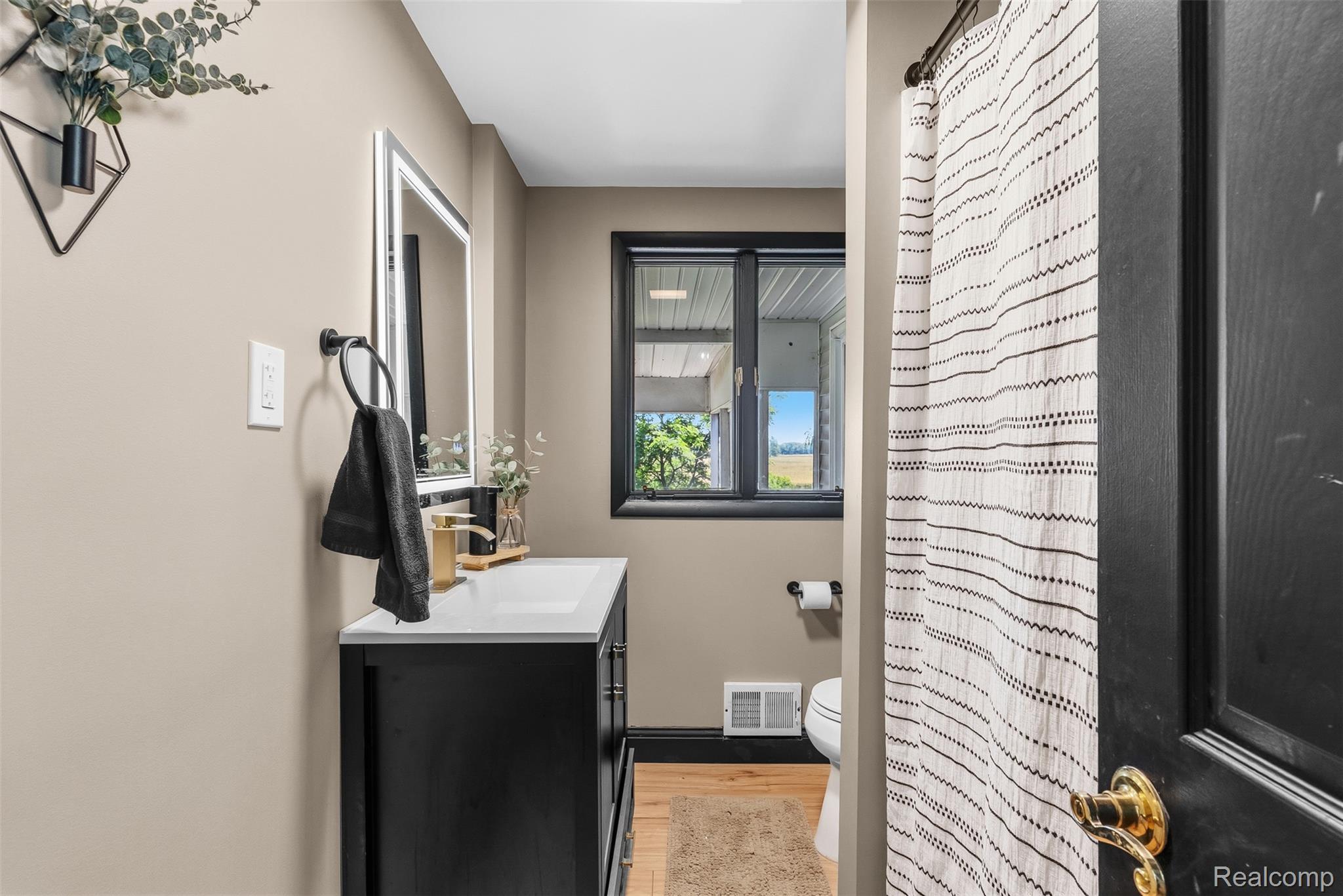 5843 West Dewey Road Owosso, MI 48867 - Photo 22 of 58 Bathroom featuring a black vanity with a white countertop, a rectangular mirror with a white frame, and a window with black trim