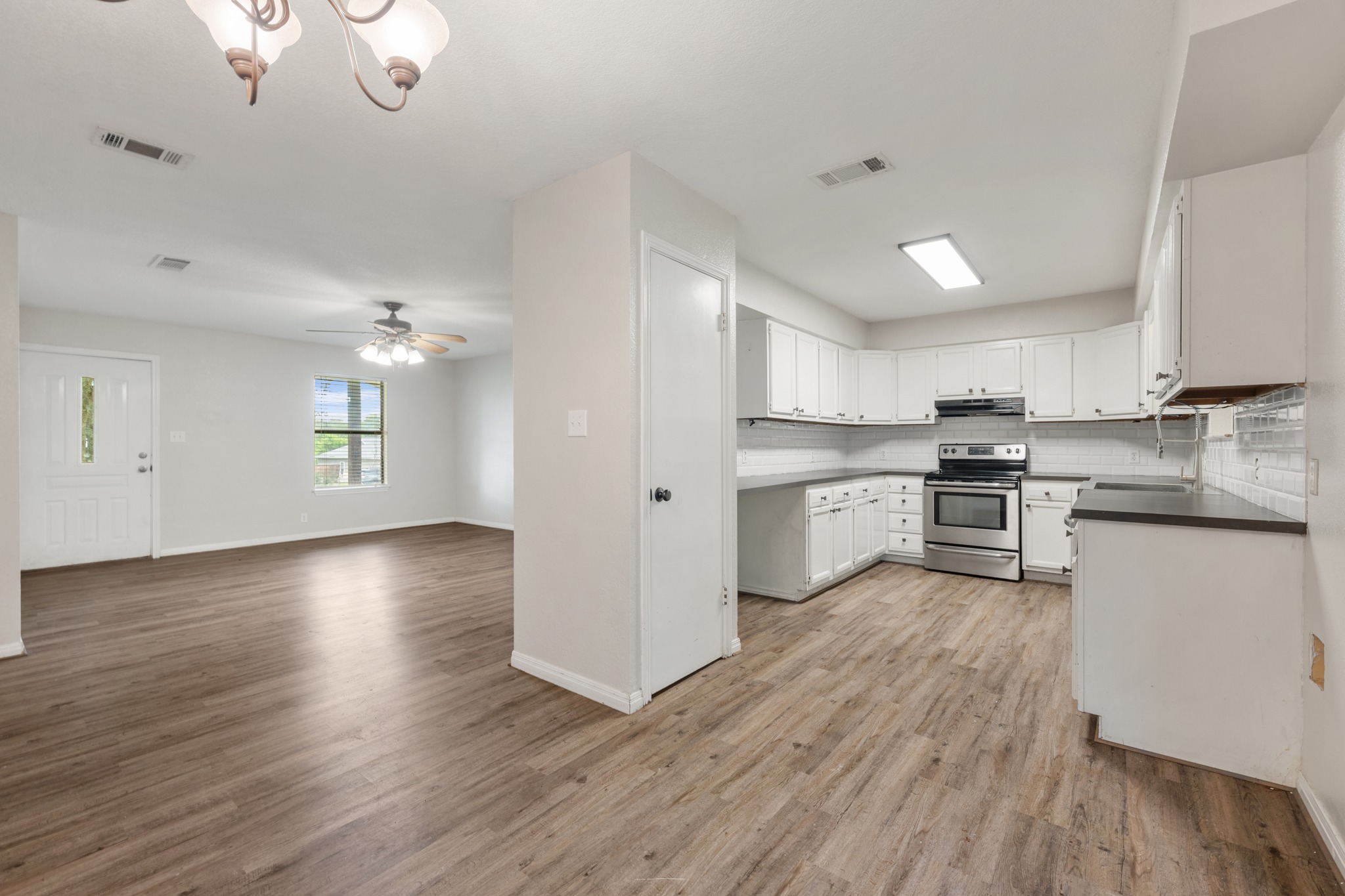 110 Skyview Terrace Leander, TX 78641 - Photo 11 of 26 Kitchen and living area featuring wood-finish flooring, white cabinetry, dark countertops, a subway tile backsplash, and stainless steel appliances