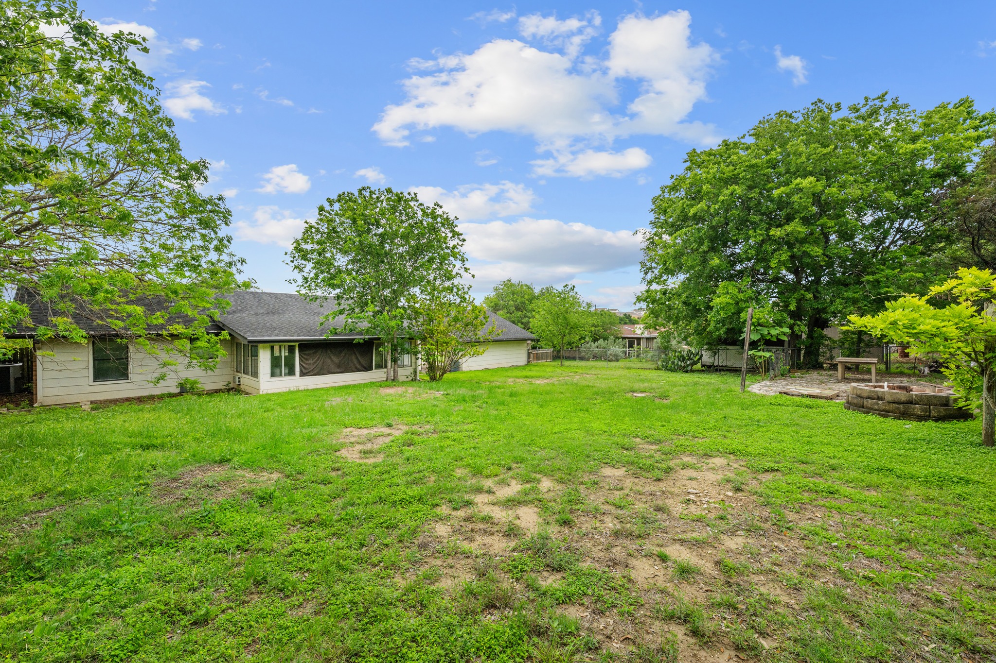 110 Skyview Terrace Leander, TX 78641 - Photo 22 of 26 Expansive grassy yard area featuring a stone fire pit with a surrounding patio, mature trees, and a screened back porch