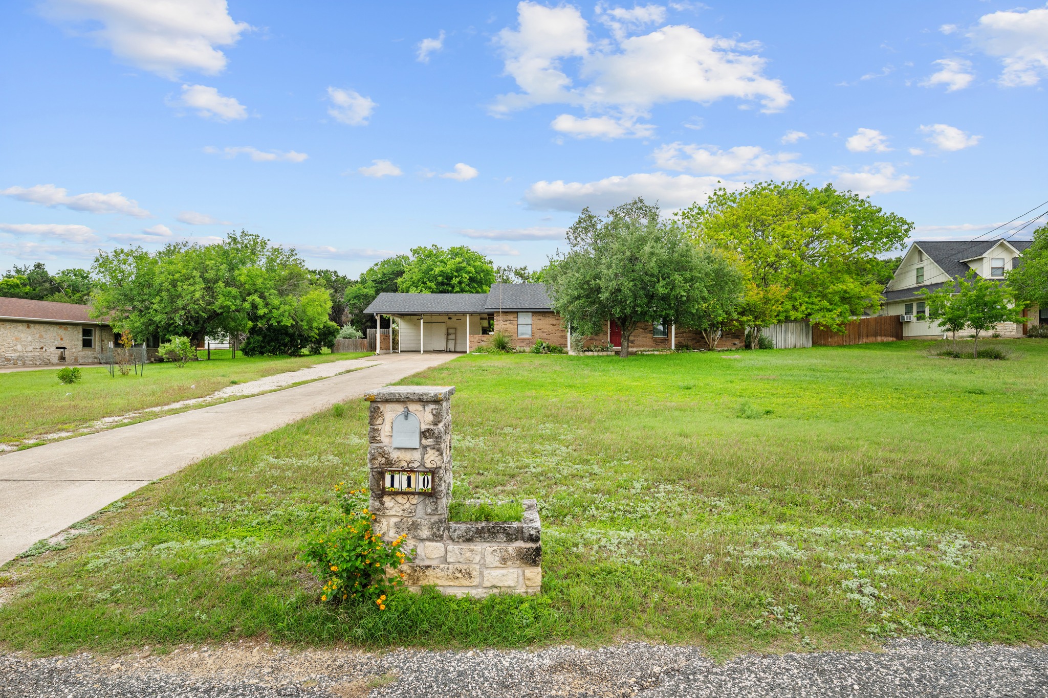 110 Skyview Terrace Leander, TX 78641 - Photo 3 of 26 Expansive front lawn with a stone-clad mailbox and long driveway leading to a single-story residence featuring a carport and mature trees