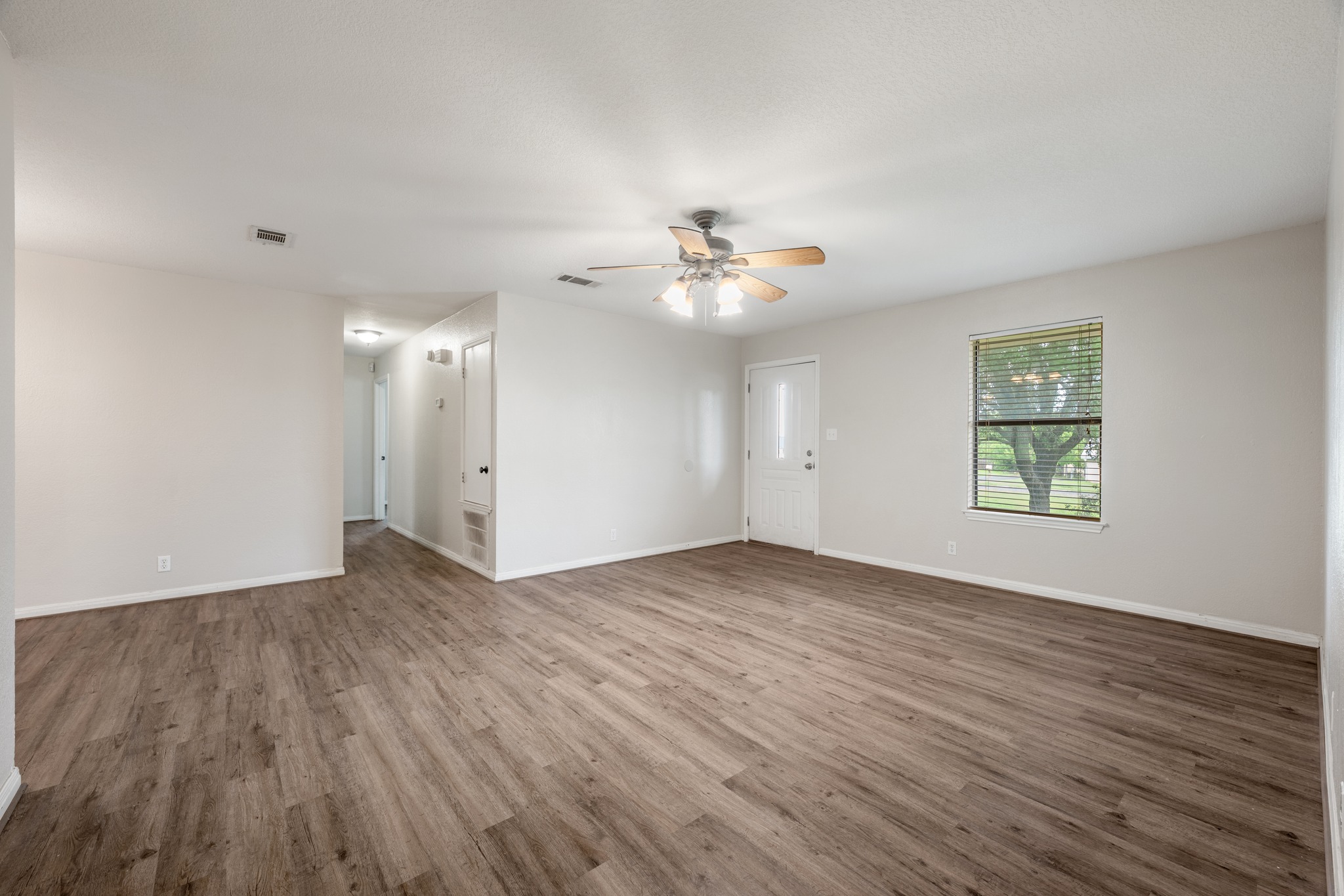 110 Skyview Terrace Leander, TX 78641 - Photo 5 of 26 Spacious room featuring wood-finish flooring, light neutral wall tones, a ceiling fan with integrated lighting, a window with blinds, and a white entry door