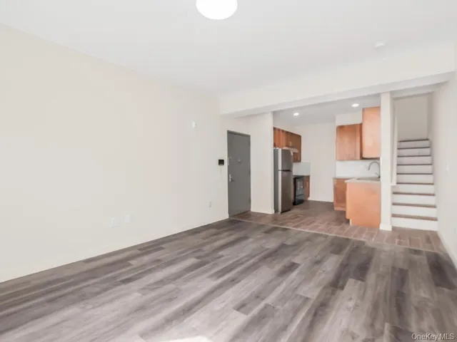 a view of empty room with wooden floor and kitchen
