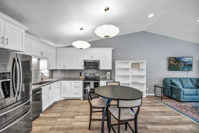 a kitchen with stainless steel appliances granite countertop a stove top oven a sink dishwasher a dining table and chairs with wooden floor