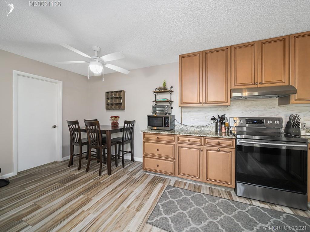 5804 Southeast Windsong Lane Stuart, FL 34997 - Photo 3 of 20 a kitchen with stainless steel appliances granite countertop a stove top oven a sink dishwasher and white cabinets with wooden floor
