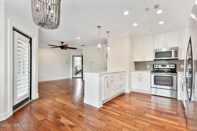 a kitchen with stainless steel appliances granite countertop a refrigerator a sink dishwasher a stove and white countertops with wooden floor