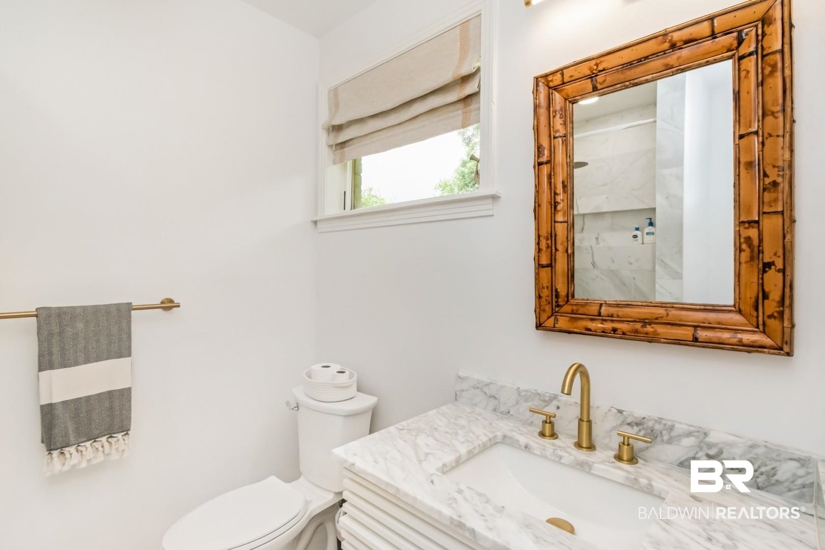 4596 Hawthorne Place Mobile, AL 36608 - Photo 20 of 34 Bathroom featuring a marble vanity with an undermount sink and brass faucet, a bamboo-framed mirror, a window with a roman shade, and a white toilet