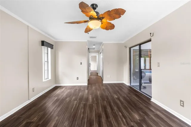 an empty room with wooden floor chandelier fan and windows